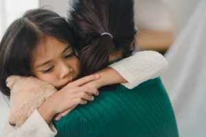 Child hugging woman while holding teddy bear, symbolizing safety and support.